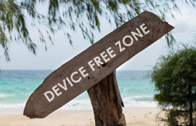 Old wooden sign with text device free zone on tropical beach. Rest from social media gadget and internet